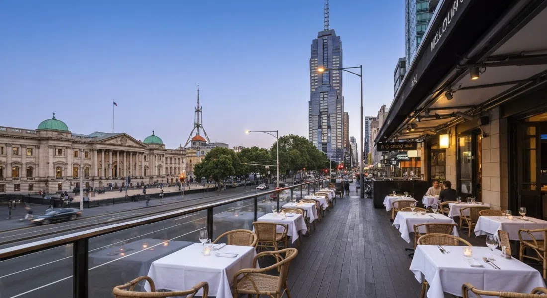 Siglo-terrassen over Melbourne Supper Club på Spring Street i skumringen, hvidklædte borde, flettede stole og Parliament House på tværs af gaden