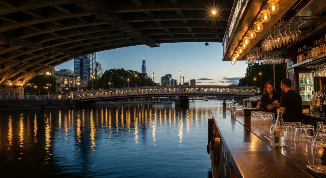 El bar en pontón de Ponyfish Island bajo el Evan Walker Bridge al atardecer, con luces cálidas reflejándose en el Yarra y copas en la barra