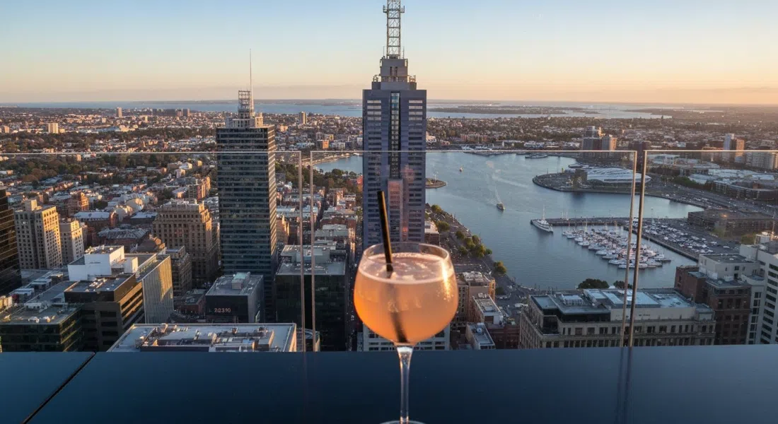 Strato Melbourne en el piso 40 al atardecer, con una copa de cóctel en primer plano y el CBD y la bahía extendiéndose abajo